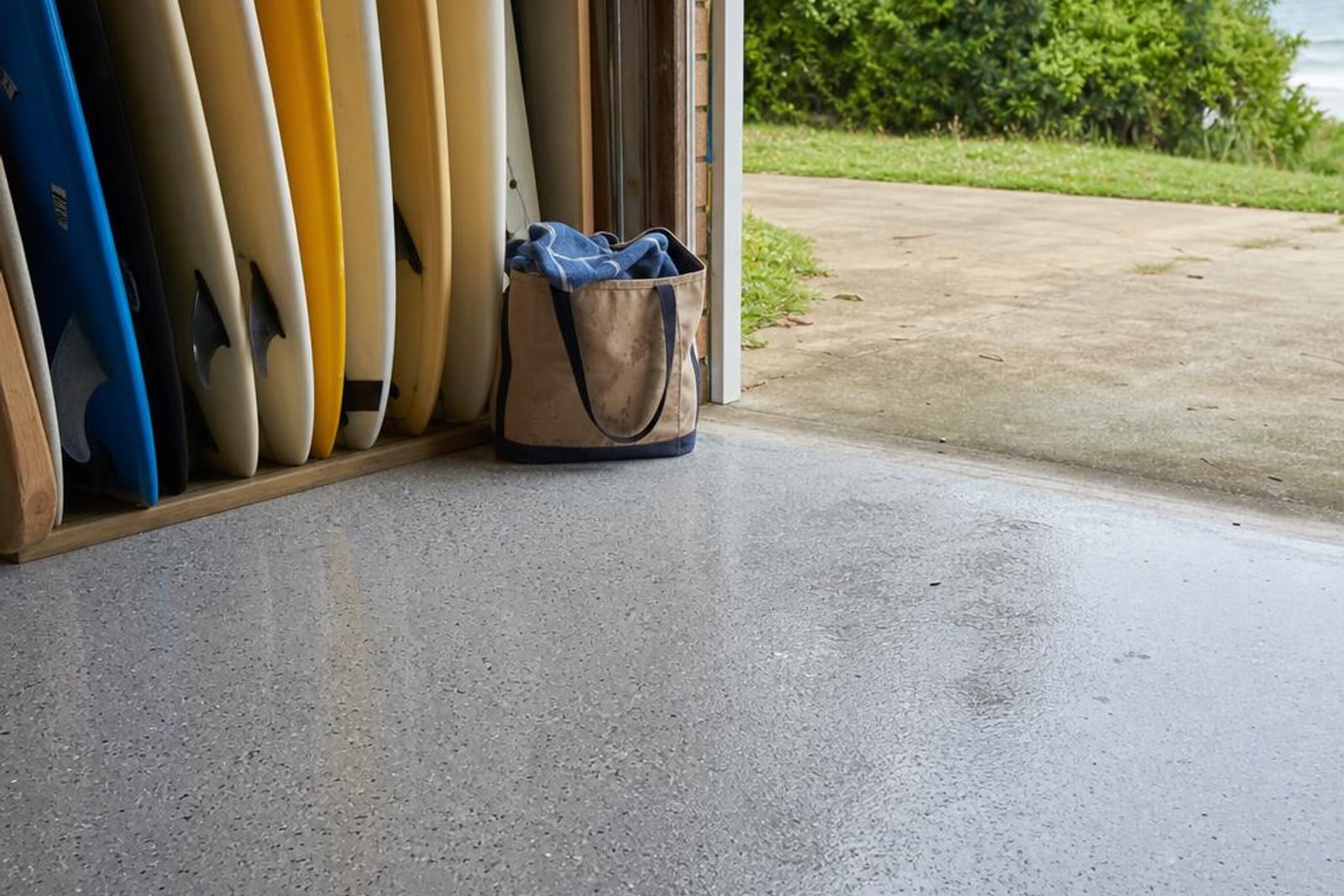 Grey flake epoxy garage floor opening toward a coastal driveway with surfboards in storage