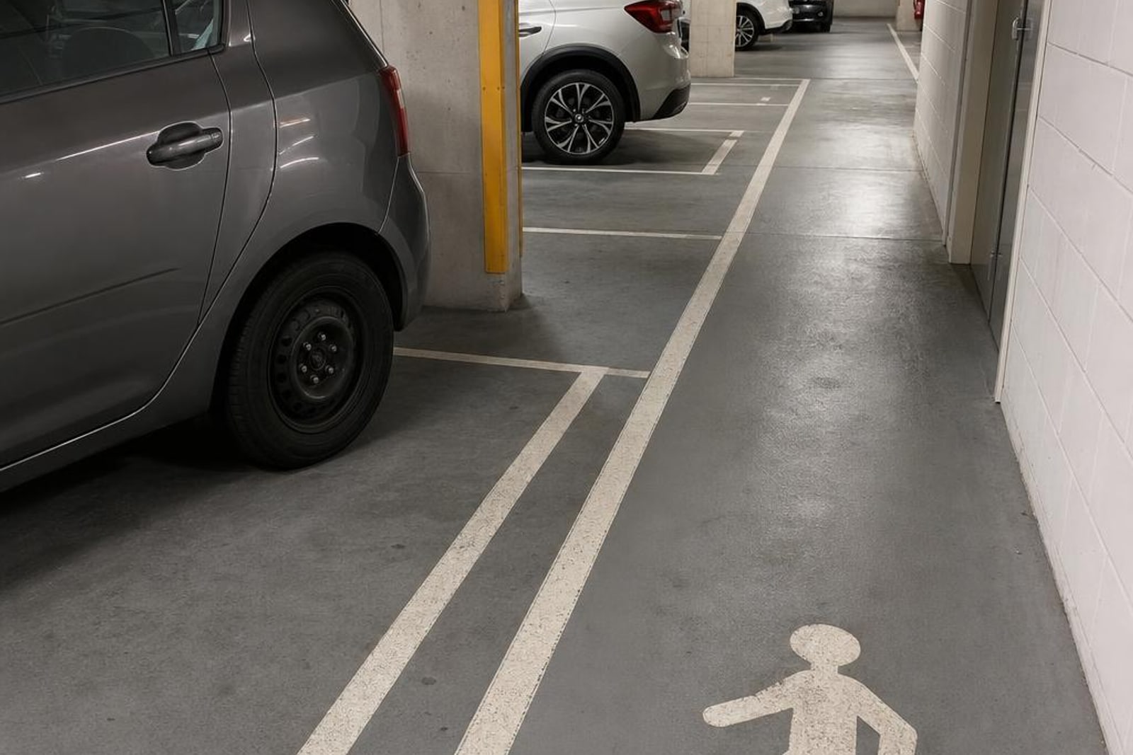 Basement shared garage parking bays and marked pedestrian route beside concrete columns