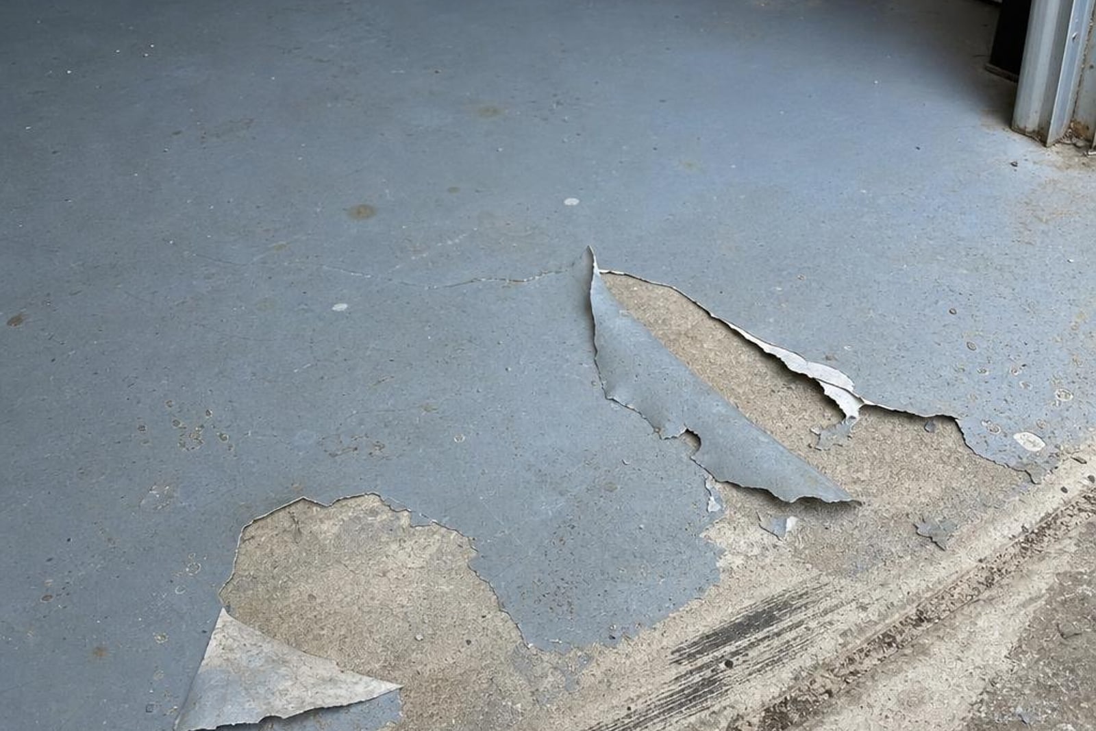 Failed grey epoxy garage coating peeling away from bare concrete
